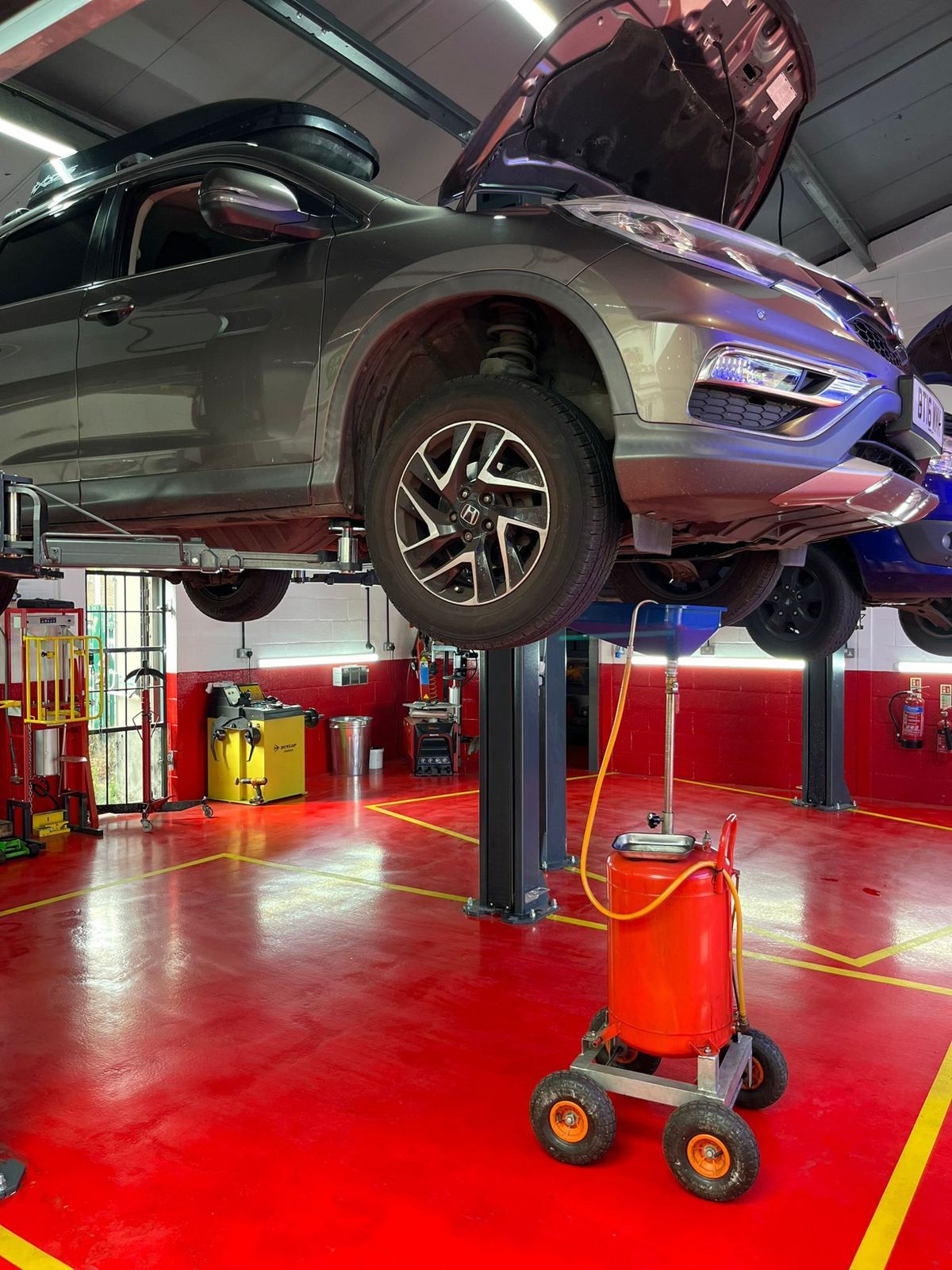 A car up on a lift with its bonnet open, mid-service, on the red workshop floor