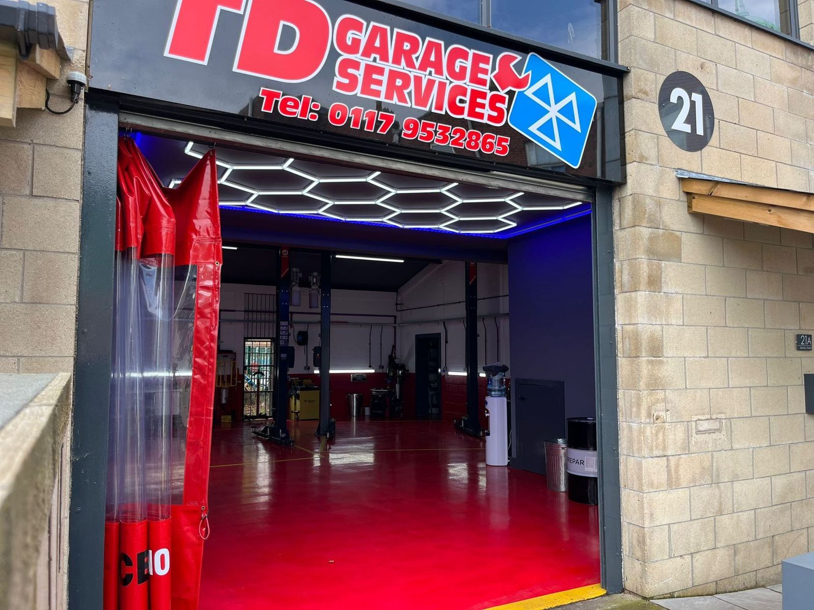 TD Garage Services from Bartley Street: the roller door open, the hexagon light ceiling on, and the red workshop floor inside