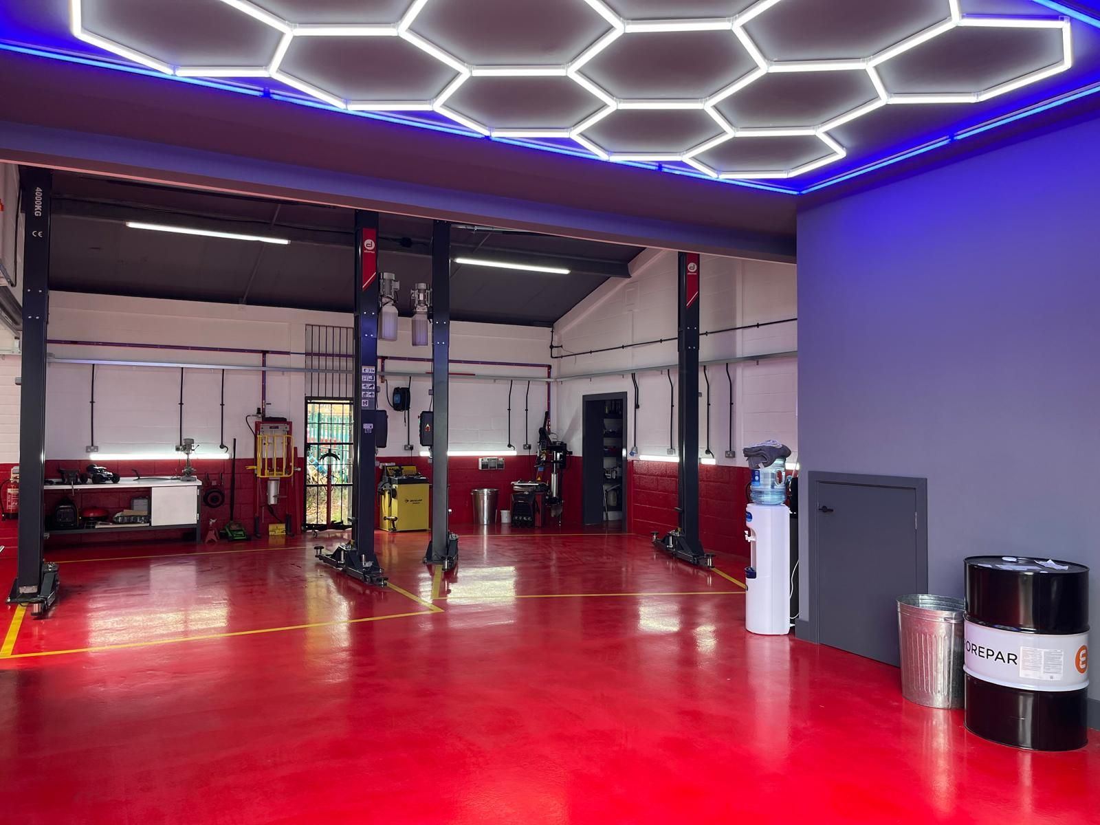 The empty workshop: glossy red floor with yellow bay lines, two-post lifts and the hexagon light ceiling