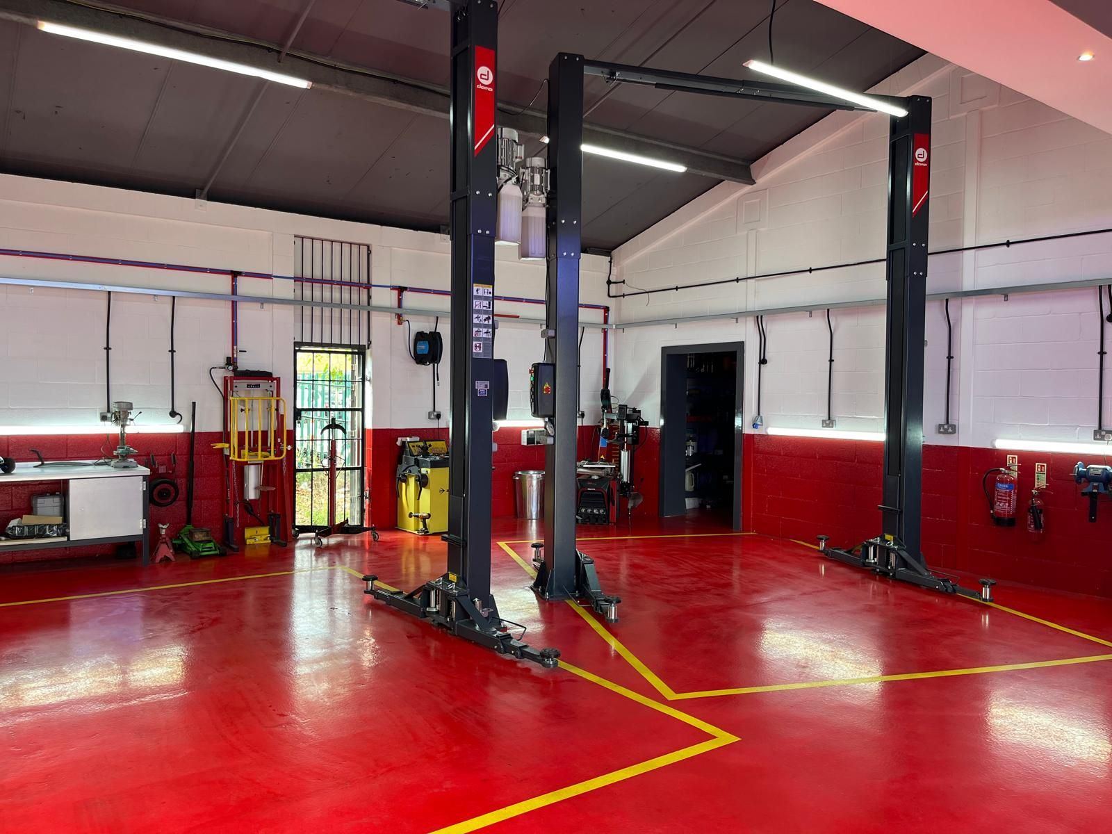 Two-post lifts on the red workshop floor with yellow bay lines